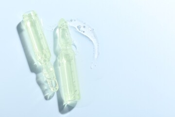 Glass ampoules with liquid on light blue background, flat lay