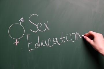 Woman writing word Sex Education on green chalkboard, closeup
