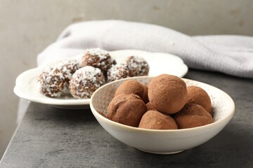 Tasty chocolate candies with cocoa powder, nuts and coconut flakes on grey table, closeup