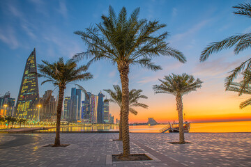 Doha city business downtown center panorama illuminated at sunrise, with modern skyscrapers and sea in the foreground, Qatar