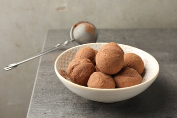 Tasty chocolate candies with cocoa powder in bowl on grey table, closeup