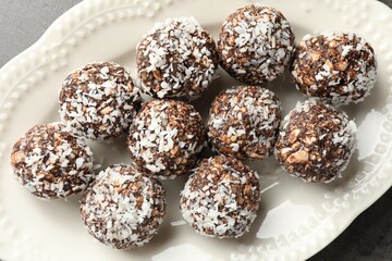 Tasty chocolate candies with nuts and coconut flakes on grey table, top view