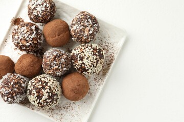 Tasty chocolate candies with cocoa powder, nuts and sesame seeds on white table, top view. Space for text