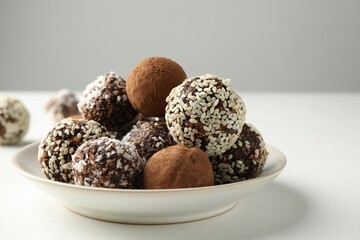 Tasty chocolate candies with cocoa powder, nuts and sesame seeds on white table, closeup