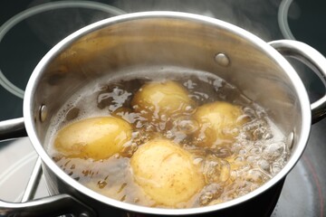 Young potatoes boiling in pot on stove, closeup