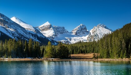 a beautiful calming photo of snow capped rocky mountains beautiful clear blue sky with a calm lake in the foreground surrounded by a forest of pine