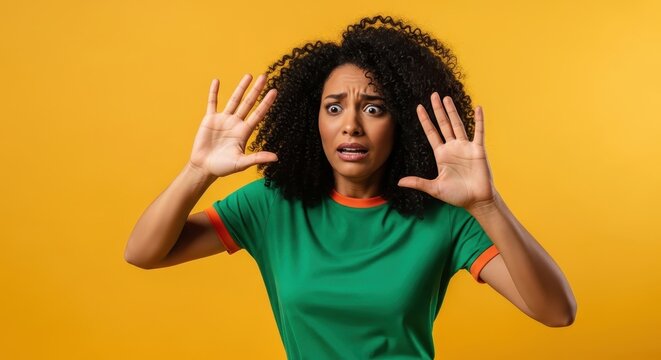 Stressed young African American woman with an anxious face, raising her hands in a protective or startled gesture on a vivid backdrop