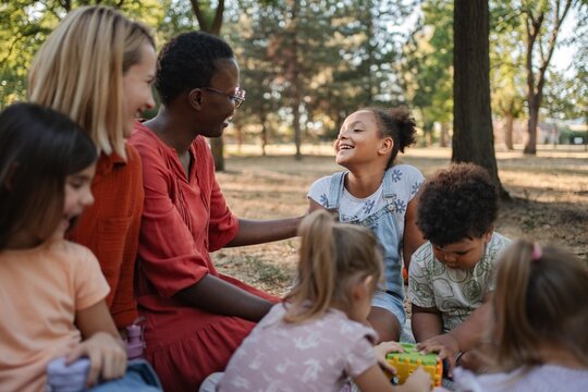 Diverse group of preschool children enjoying playtime with their teachers in a park - Powered by Adobe