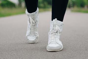young slim beautiful caucasian woman running on path on river embankment in city park, black sportswear, white sneakers close-up view, warm summer day
