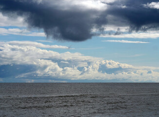 Stormy sky over the sea - Dramatic weather approaching coast - A dramatic seascape with a large, dark storm cloud looming above the calm sea and white clouds