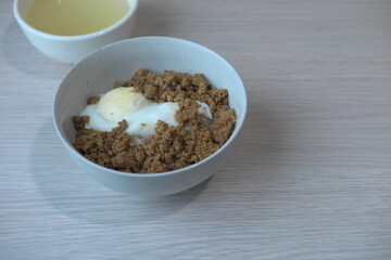 A comfort food bowl with minced meat and a half-boiled egg, a simple and nutritious meal. A small bowl of clear soup is visible in the background, completing a classic Asian meal.