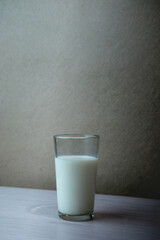 A clear glass filled with fresh milk placed on a wooden table against a simple wall background, representing healthy dairy drink and natural nutrition.