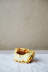A half-eaten Portuguese pastel de nata egg tart pastry with a bite taken out, served on a wrinkled white paper with a light, simple background.