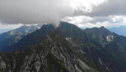 Fototapeta premium A majestic mountain range is partially obscured by low-hanging clouds, showcasing the rugged terrain and natural beauty of the landscape.