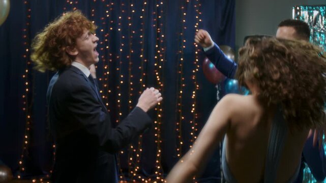 Young attractive girl in eening dress dancing energeically together with two o her classmates at high scool prom party