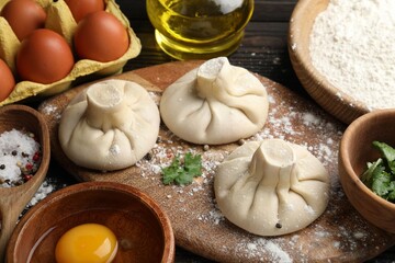 Uncooked khinkalis (dumplings) surrounded by ingredients on wooden table, closeup