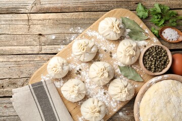 Uncooked khinkalis (dumplings) with peppercorns, flour, parsley and bay leaves on wooden table, flat lay