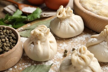 Uncooked khinkalis (dumplings) with peppercorns, flour and bay leaves on wooden table, closeup