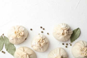 Uncooked khinkalis (dumplings) with peppercorns and bay leaves on white table, flat lay. Space for text