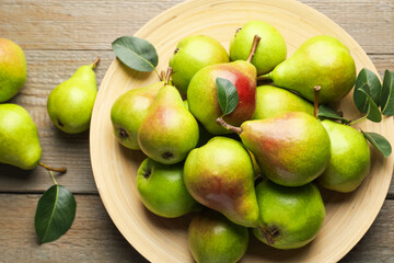 Fresh ripe pears and green leaves on wooden table, flat lay