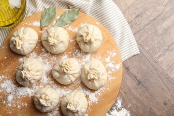Uncooked khinkalis (dumplings) with flour, oil and bay leaves on wooden table, top view. Space for text