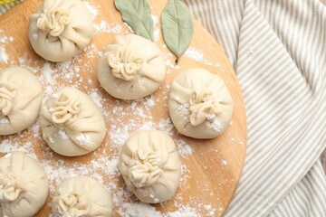 Uncooked khinkalis (dumplings) with flour and bay leaves on table, top view