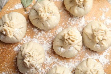 Uncooked khinkalis (dumplings) with flour on wooden board, top view