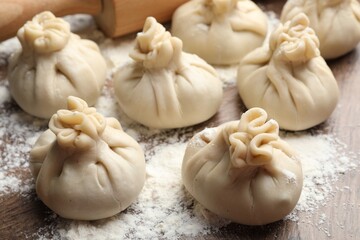 Uncooked khinkalis (dumplings) with flour on wooden table, closeup