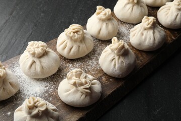 Uncooked khinkalis (dumplings) with flour on black table, closeup
