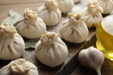 Uncooked khinkalis (dumplings) with flour, garlic and bay leaves on wooden table, closeup