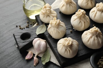 Uncooked khinkalis (dumplings) with peppercorns, garlic and bay leaves on black table, closeup