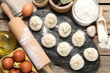 Uncooked khinkalis (dumplings), flour, spices, eggs and rolling pin on wooden table, flat lay
