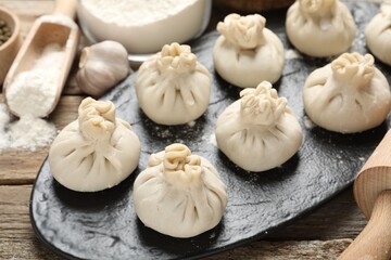 Uncooked khinkalis (dumplings), flour, garlic and rolling pin on wooden table, closeup