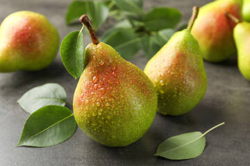Fresh ripe pears and green leaves on grey table, closeup