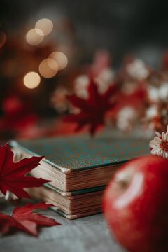 Pomme rouge tombant d&rsquo;une pile de livres entour&eacute;e de fleurs et feuilles d&rsquo;automne, ambiance chaleureuse illustrant la rentr&eacute;e scolaire