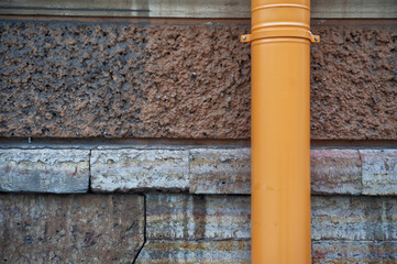 Orange drainpipe contrasts with textured stone wall facade