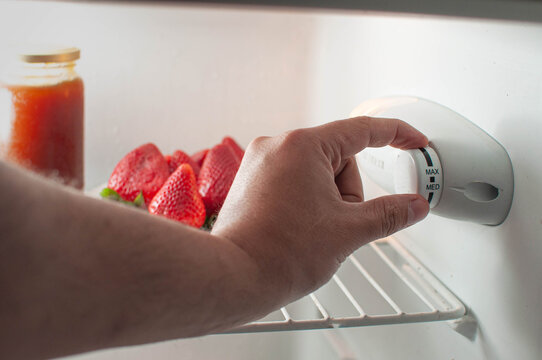 mano cambiando el termostato de la nevera. modificando la temperatura. consumo de energ&iacute;a, frutillas de fondo