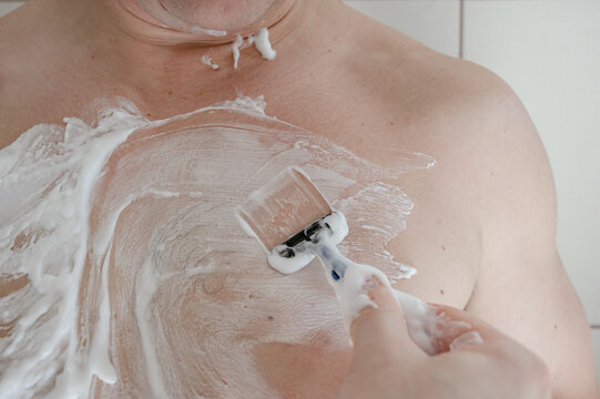 Close-up of man shaving his body with razor and foam, concept of male grooming and personal care.