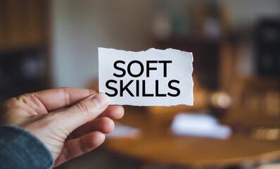 A hand holding a piece of white paper with the text soft skills written on it