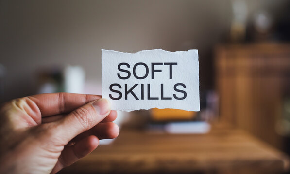 A hand holding a piece of white paper with the text soft skills written on it