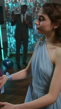 Vertical shot of young giir in blue evening dress holding hands and slow dancing with unrecognizable red-hared boyfriend at high schol prom party