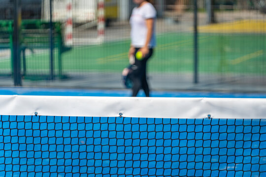 Paddle tennis net with player holding racket and balls in background