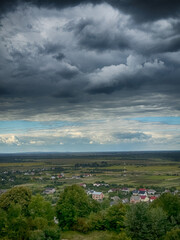 Hilltop view of village under dramatic cloudy sky. Scenic panorama of countryside village before the rain
