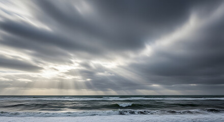 Dramatic seascape with sun rays piercing through turbulent cloudy sky over ocean