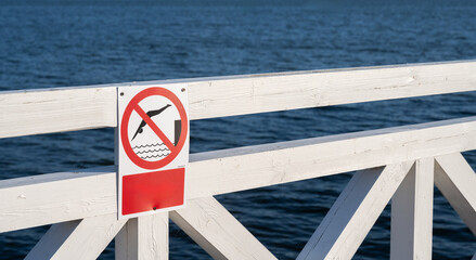 No diving sign on pier railing with water surface in background – safety warning at lake or...