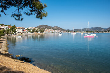 Scenic coastal view of Ermioni Greece with calm blue sea, anchored sailboats, hillside houses, and clear summer sky