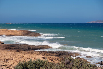 Gavdos island, Greece. Rocky coastline with sparse vegetation and sea waves, blue sky, summer sunny day