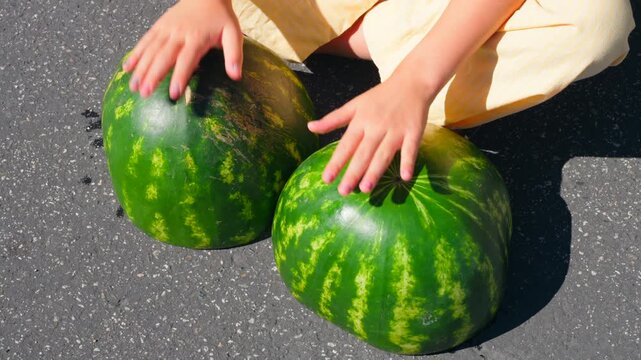 Close up shot of a young girl sitting on the ground having fun with make-believe, playing watermelon halves as bongo drums.