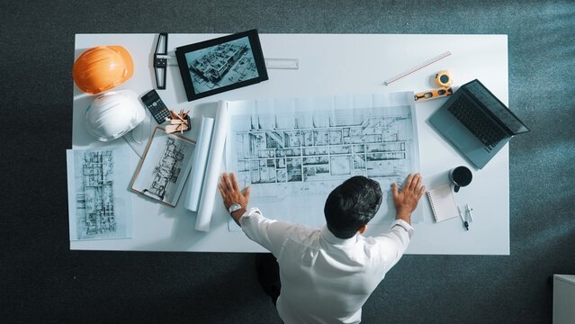 Top down view of skilled engineer looking at blueprint at meeting. Aerial view of architect checking project plan and prepare for measuring building blueprint while standing at meeting. Alimentation.
