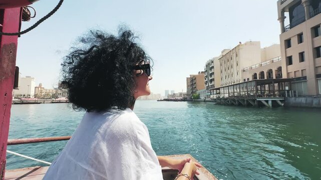 Stylish fashion business woman enjoying a abra boat ride along Dubai Creek under clear skies